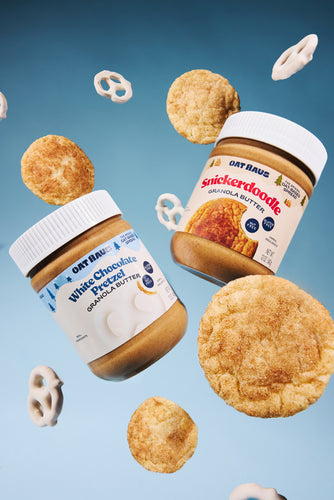 White Chocolate Pretzel Granola Butter Jar with a Snickerdoodle Granola Butter Jar floating with snickerdoodle cookies and white chocolate pretzels against a blue background. 